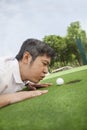 Mid adult man lying down in a golf course trying to blow the ball into the hole Royalty Free Stock Photo