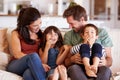 Mid adult white couple and their two young children sitting on a sofa at home smiling at each other Royalty Free Stock Photo