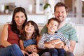 Mid adult white couple and their two young children sitting on a sofa at home smiling to camera Royalty Free Stock Photo