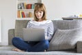 Mid adult woman on her sofa using laptop at home. Royalty Free Stock Photo