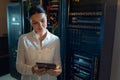 Mid-adult woman using tablet while checking network cables in server room, with blinking LEDs Royalty Free Stock Photo