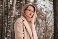 Mid age woman in finter forest looking at camera. Blonde girl in coat eyeglasses and sweater outdoors Royalty Free Stock Photo