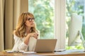 Mid aged blond haired woman sitting at table and using laptop and computer for work Royalty Free Stock Photo