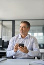 Mid aged happy business man using mobile phone in office thinking, vertical. Royalty Free Stock Photo