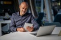 Mid aged professional man sitting at the office and using touchpad and notebook for work