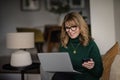 Mid aged woman sitting at home and using laptop and smartphone for work Royalty Free Stock Photo