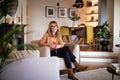 Mid aged woman using earphones and cellphone and sitting in an armchair at home Royalty Free Stock Photo