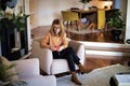 Mid aged woman using earphones and cellphone and sitting in an armchair at home Royalty Free Stock Photo