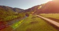 Mid air flight over fresh mountain river and meadow at sunny summer morning. Rural dirt road below. Royalty Free Stock Photo
