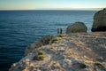 Mid distance view of couple standing on cliff by seascape against sky at sunset