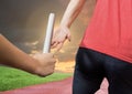 Mid-section of athlete passing the baton to teammate in stadium at sunset