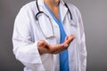 Mid section of female doctor with cupped hand against grey background