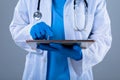 Mid section of female doctor using digital tablet against grey background