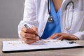 Mid section of female doctor writing on clipboard against grey background