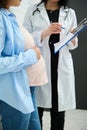 Mid-section image. Unrecognizable female doctor explaining ultrasound scan results to pregnant woman in obstetric clinic