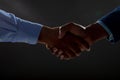 Mid section of two businessmen shaking hands against black background
