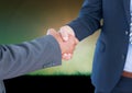 Mid section of two businessmen shaking hands against grass in background