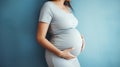 Mid-section of unrecognizable pregnant woman smiling and holding her big belly caringly against blue wall of childrens room. Royalty Free Stock Photo