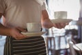 Mid section of waiter holding coffee cups in cafe