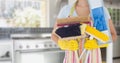 Mid section of woman holding various cleaning equipments in kitchen