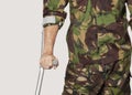 Mid section of young soldier holding crutches against gray background