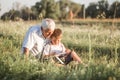 Mid shot of grandfather and his grandson while reading a book together in meadow Small boy making first steps in read