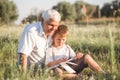 Mid shot of grandfather and his grandson while reading a book together in meadow Small boy making first steps in read