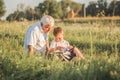 Mid shot of grandfather and his grandson while reading a book together in meadow Small boy making first steps in read
