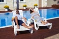 Happy couple lying on lounge chairs in front of house with pool Royalty Free Stock Photo