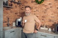 A midagedman standing in the kitchen with a coffee cup in hands