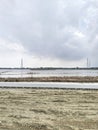 The midday sun shines on the water surface in the rice fields, which have a wire mesh barrier between the concrete and sand.