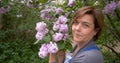 Middl aged woman smiles in the park near lilac flowers.