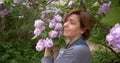 Middl aged woman smiles in the park near lilac flowers. T