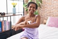 Middle age african american woman applying skin treatment sitting on bed at bedroom Royalty Free Stock Photo