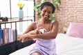 Middle age african american woman applying skin treatment sitting on bed at bedroom Royalty Free Stock Photo