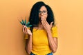 Middle age african american woman holding picklock to unlock security door covering mouth with hand, shocked and afraid for