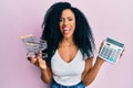 Middle age african american woman holding small supermarket shopping cart and calculator smiling and laughing hard out loud