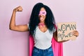 Middle age african american woman wearing super hero costume holding woman power banner sticking tongue out happy with funny