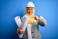 Middle age architect woman wearing muslim hijab and security helmet holding blueprints very happy pointing with hand and finger