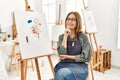 Middle age artist woman at art studio looking confident at the camera smiling with crossed arms and hand raised on chin Royalty Free Stock Photo