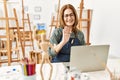 Middle age artist woman smiling happy having video call using laptop at art studio Royalty Free Stock Photo