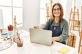 Middle age artist woman smiling happy using laptop at art studio Royalty Free Stock Photo