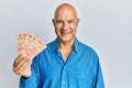 Middle age bald man holding mexican pesos looking positive and happy standing and smiling with a confident smile showing teeth
