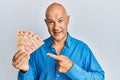 Middle age bald man holding mexican pesos smiling happy pointing with hand and finger
