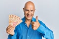 Middle age bald man holding mexican pesos smiling happy and positive, thumb up doing excellent and approval sign