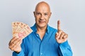 Middle age bald man holding mexican pesos smiling with an idea or question pointing finger with happy face, number one