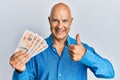 Middle age bald man holding 10 united kingdom pounds banknotes smiling happy and positive, thumb up doing excellent and approval Royalty Free Stock Photo