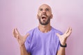 Middle age bald man standing over pink background crazy and mad shouting and yelling with aggressive expression and arms raised