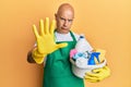 Middle age bald man wearing cleaner apron holding cleaning products with open hand doing stop sign with serious and confident Royalty Free Stock Photo