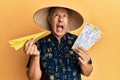 Middle age bald man wearing traditional asian hat holding boarding pass angry and mad screaming frustrated and furious, shouting Royalty Free Stock Photo